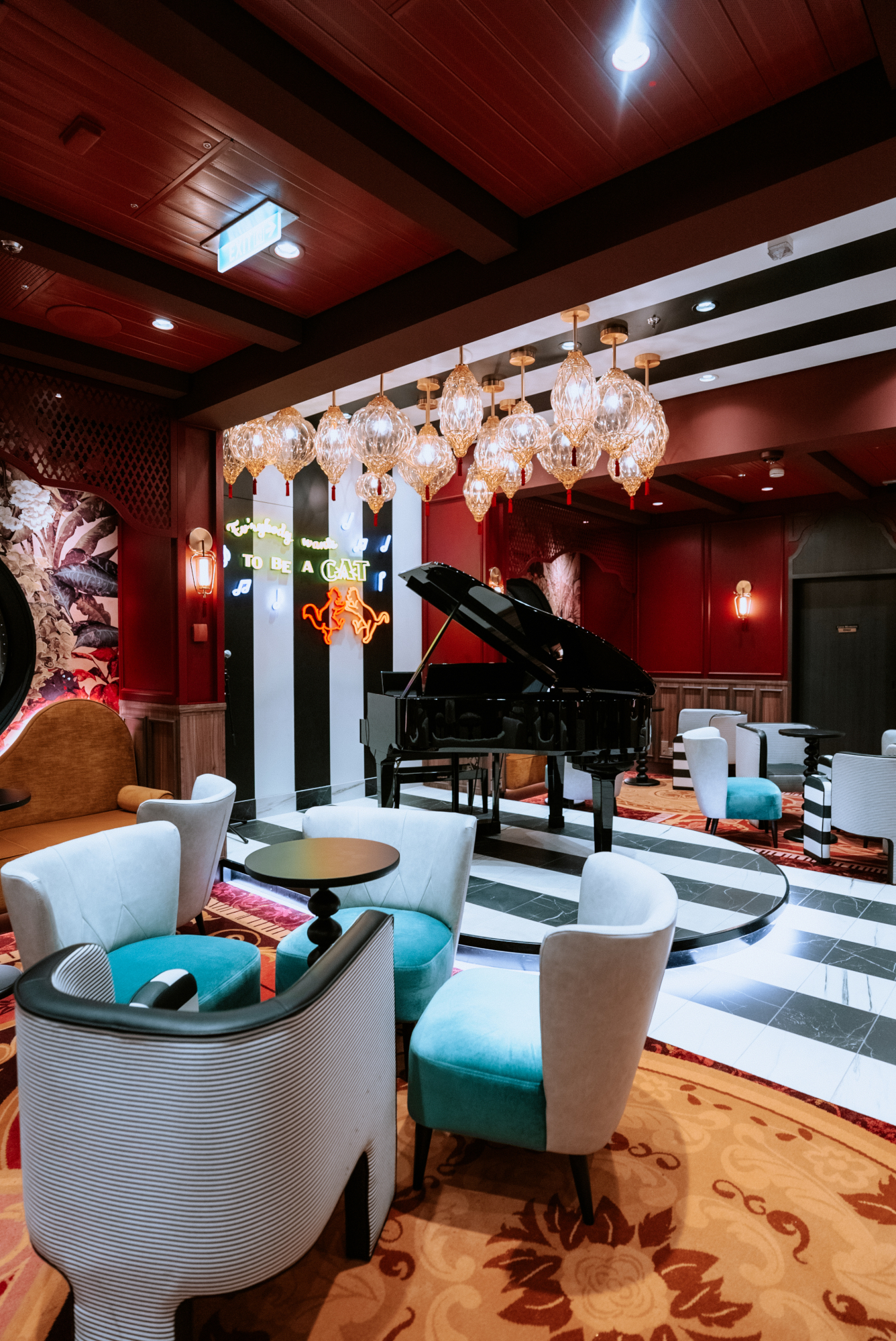 A cruise ship piano lounge features upholstered chairs, patterned carpet, and hanging glass lights