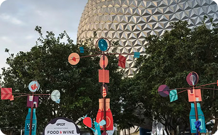 Colorful festival decorations stand among trees in front of Spaceship Earth at EPCOT