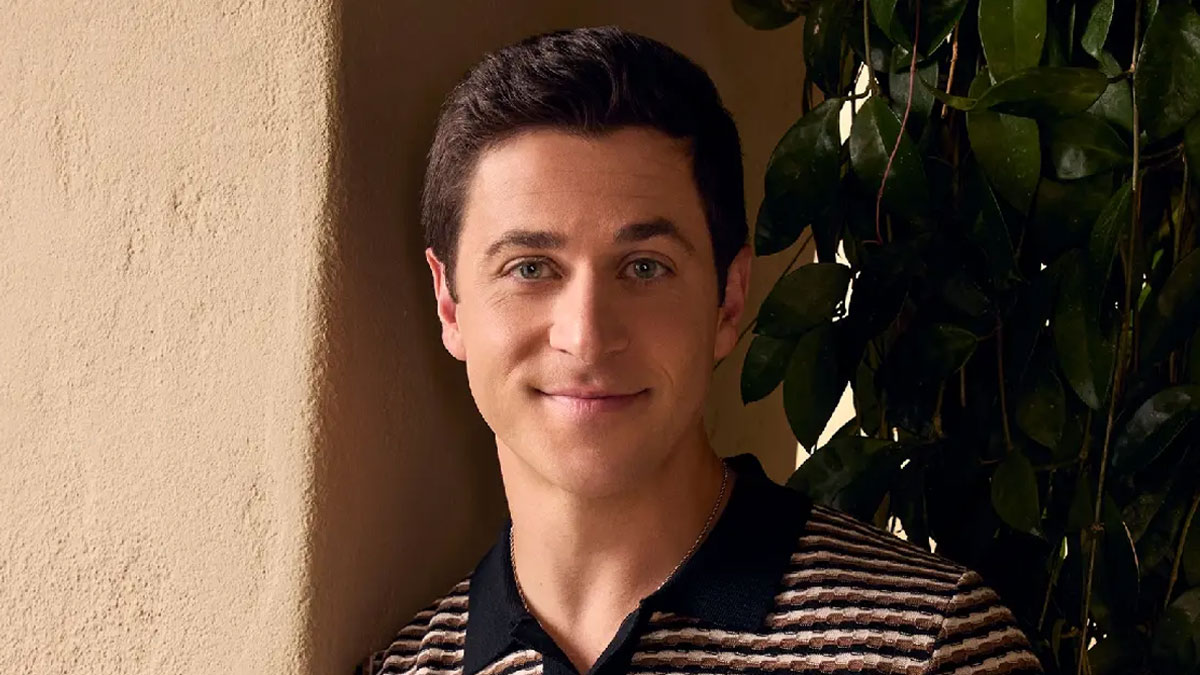Portrait of David Henrie beside a sunlit wall and leafy plants