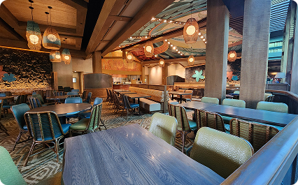 A tropical resort lounge has wooden tables, cushioned seating, and hanging lanterns