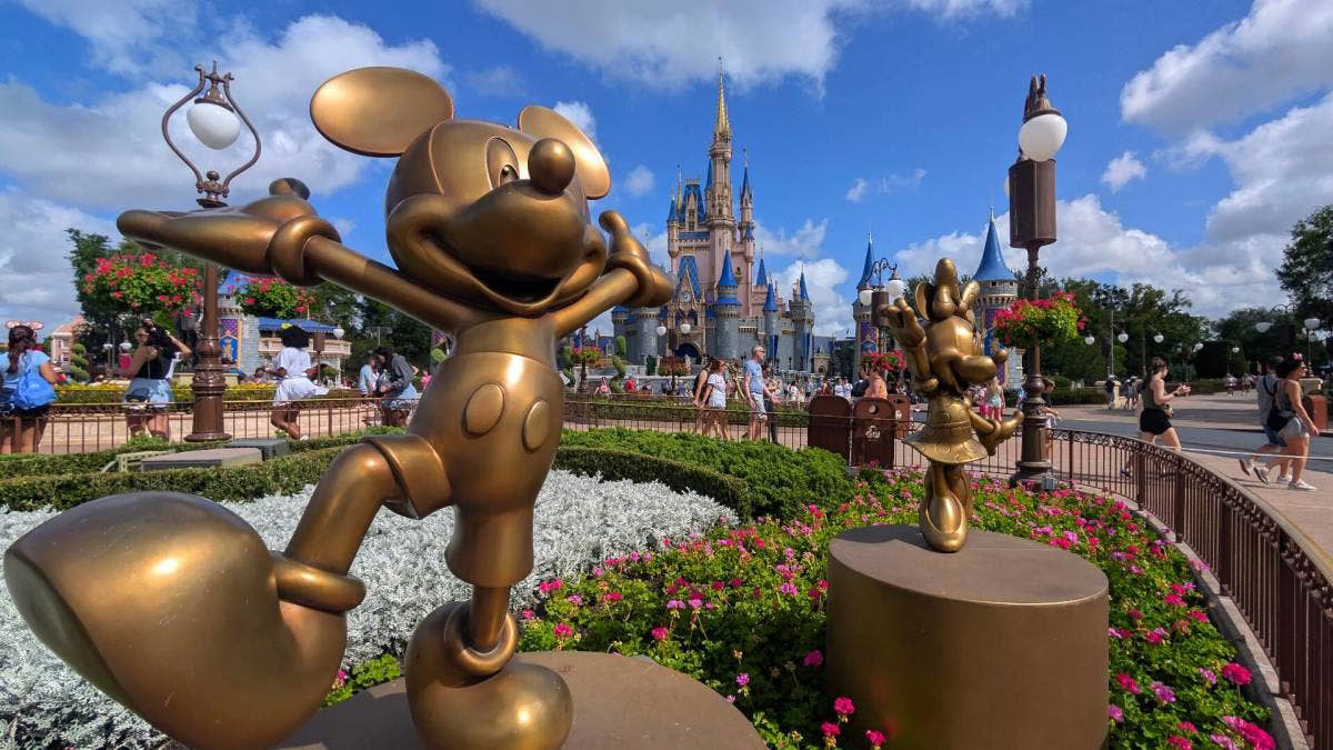 A golden Mickey Mouse statue stands among flowers with Cinderella Castle in the distance