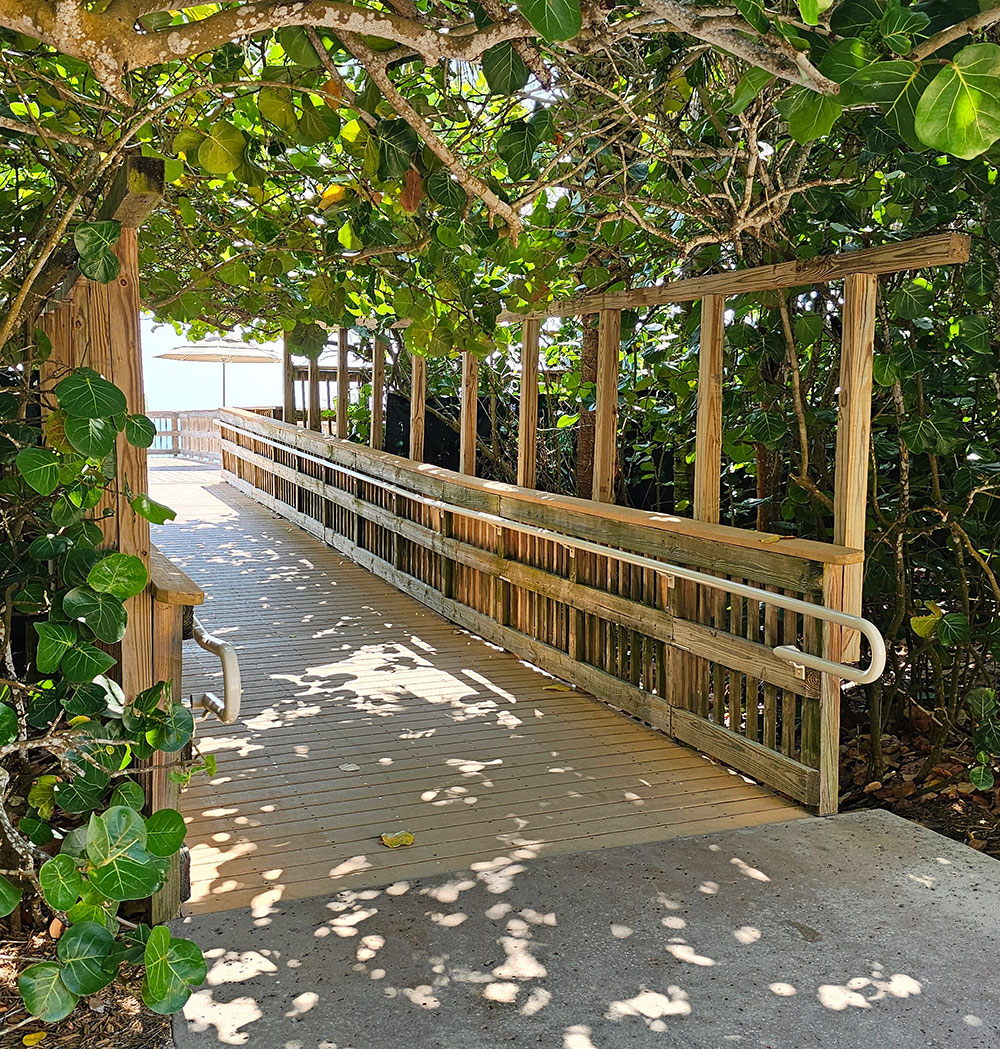 A wooden footbridge crosses a shaded path beneath leafy trees